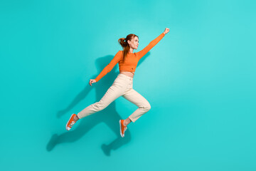 Obraz premium Full length photo of strong woman wear crop top white pants raising fist up fly to empty space isolated on turquoise color background