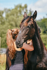 Girl cuddling with black horse in summer