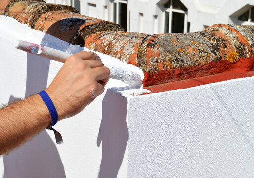 Pintor pintando a mano con brocha y pintura impermeabilizante de caucho blanco la uni&oacute;n del muro antepecho de la terraza con las tejas. 
