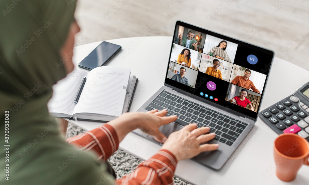 Poster a woman in a green hijab is sitting at a desk with a laptop. she is looking at the screen which is s