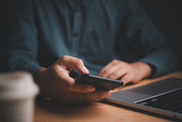 Businessman using smartphone at desk, laptop nearby. Represents digital communication, multitasking. Ideal for tech, corporate themes.