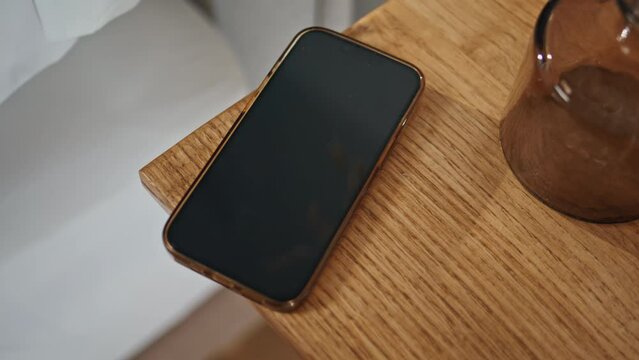 Closeup smartphone wooden table in ambient bedroom setting. Locked smart device