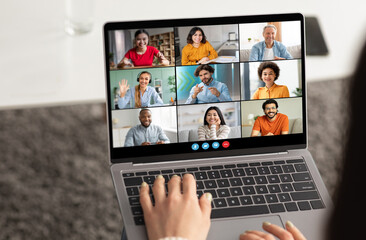 A woman is typing on a laptop computer, participating in a video conference with eight other...