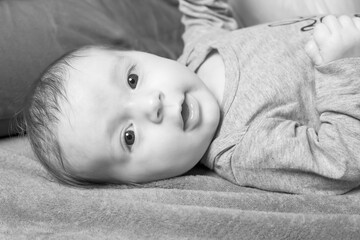 Black and white side view photo of  cute baby boy lying on the blanket. 