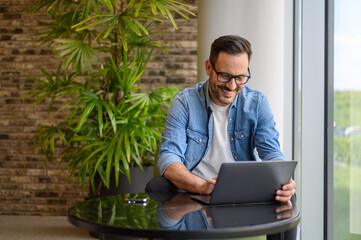 Portrait of confident positive male manager checking e-mails over laptop on table in modern office