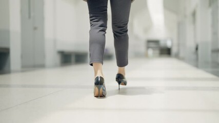 A woman wearing high heels walks down a hallway. Concept of elegance and sophistication, as the woman's attire and posture suggest that she is attending a formal event or going to work