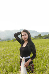 portrait of an Indonesian woman wearing a black Balinese kebaya in a rice field in a random pose...