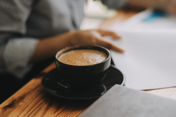 closeup hands of business woman in pastel pink shirt working on laptop and making notices in her notebook on wooden table with a cup of coffee