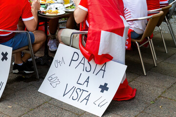 Schweizer Fans in Berlin beim Essen mit lustigem Schild in italienisch 