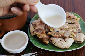 Pour coconut milk over grilled bananas cut into pieces in banana leaf-patterned plates. on the brown wooden table