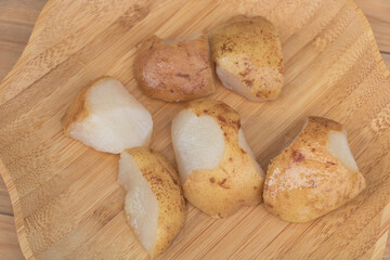 Four large potatoes and one small potato cut into pieces on a wooden plate.