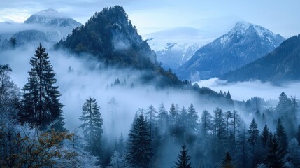 Misty mountain range with snow-capped peaks and dense forest in autumn.