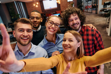 A diverse group of business professionals take a break from their tasks in a modern startup office to capture a creative selfie, showcasing teamwork and a vibrant workplace culture
