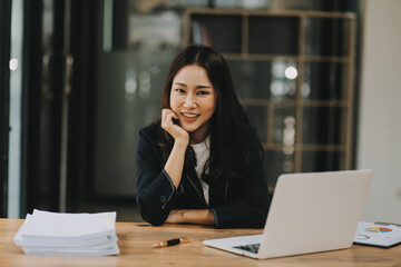 Cheerful business lady working on laptop in office, Asian happy beautiful businesswoman in formal suit work in workplace. Attractive female employee office worker smile.