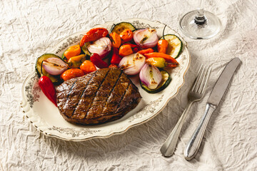 beef steak with grilled vegetables on vintage ceramic plate with fork and knife
