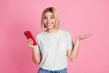 Photo of confused clueless woman with bob hairdo dressed t-shirt holding smartphone shrug shoulders isolated on pink color background