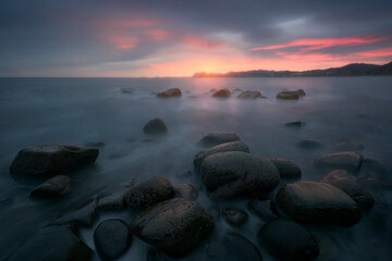 Sunrise on Arribolas beach, Bermeo, with the warm light of the sun reflected in the water and the rocks on the shore