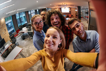 A diverse group of business professionals take a break from their tasks in a modern startup office to capture a creative selfie, showcasing teamwork and a vibrant workplace culture