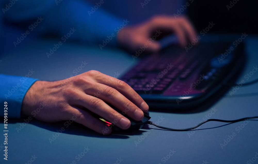 Poster A close-up image of a persons hand using a computer mouse. The hand is in focus, while the keyboard and the persons other hand are out of focus. The lighting is dim, suggesting it is nighttime.
