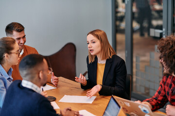 In the vibrant ambiance of a modern startup office, a diverse team of business professionals engage in discussions on various projects and develop new business strategies, epitomizing creativity and