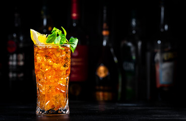 Boston ice tea, summer cocktail drink with rum, gin, vodka, tequila, liquor, juice, cola, lemon and ice in glass, dark bar background