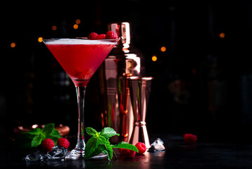 Summer red  cocktail with gin, raspberry syrup, lime juice, quail egg white and ice in glass. Black bar counter background