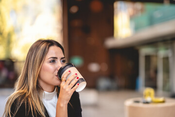 Coffee break in a public city spot: beautiful and relaxed blonde latina executive sipping coffee