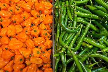 pile of bright orange habanero peppers on the left and a pile of green serrano peppers on the right