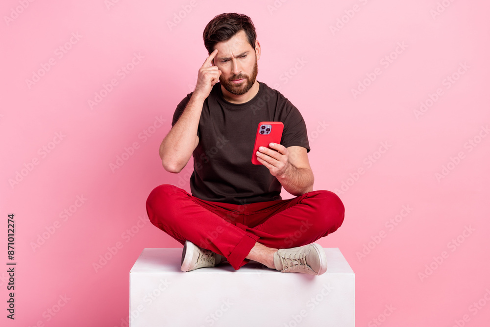 Poster full size photo of smart man dressed brown t-shirt sit on cube look at smartphone finger on forehead