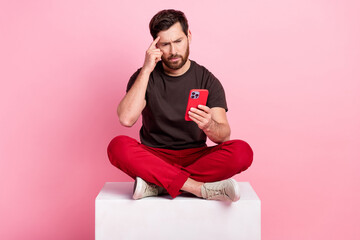 Full size photo of smart man dressed brown t-shirt sit on cube look at smartphone finger on...