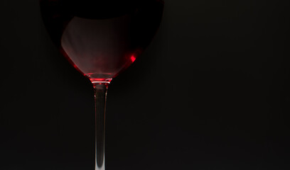 Glass of red wine close-up on black background with light reflections in natural conditions