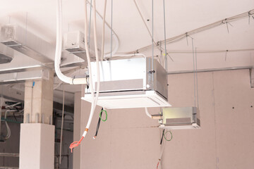 installation of industrial air conditioner hanging from the ceiling in a commercial building with electrical cables and ducts.
