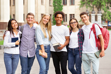 Diverse students in campus, posing in front of university and looking at camera