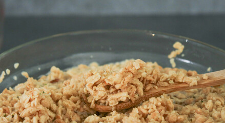 Close up of soy bean meat mince sucked up in water on a wooden spoon and glass bowl, grey marble kitchen table