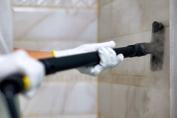 A woman wearing white gloves is meticulously steam cleaning tiles in a bathroom. The professional...