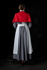 World War 1 nurse wearing a grey dress, white apron, and a red cape