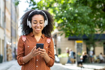 Smiling woman listening to music on headphones while using smartphone outdoors