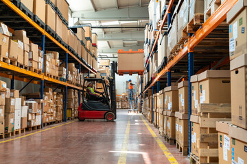 Manager wearing hard hat with digital tablet counts merchandise in warehouse. He walks through rows of storage racks with merchandise. © bulentbaris