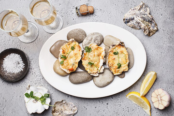 Baked stuffed oysters decorated with micro greens served on gray stones with two glasses of...
