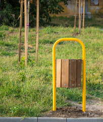 Yellow metal and wood trash can in a park with green grass