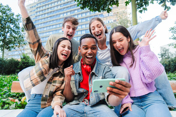 Group of young teenage students looking at their notes on the internet using a cellphone and...