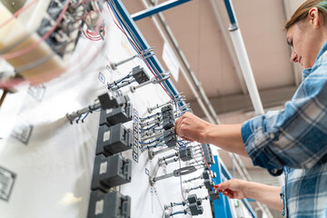 A female engineer in a work wear is working on manufacturing of home appliances factory an electrical control panel.