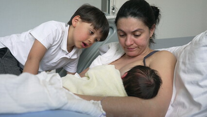 Mother breastfeeding newborn baby with older sibling observing, highlighting the nurturing bond and family interaction, suitable for family and parenting themes