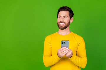 Photo portrait of handsome young guy look empty space hold device dressed stylish yellow garment isolated on green color background