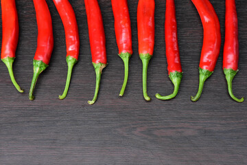Chilli red peppers border isolated on black wooden background. Bunch of long red hot peppers, aligned in a horizontal row frame