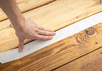 A hand carefully presses painters tape onto a wooden surface, creating a clean, straight line.
