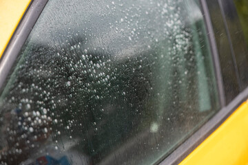 A close-up shot of a car window covered in soapy water beads during a car wash. The bubbles create a shimmering, iridescent effect.