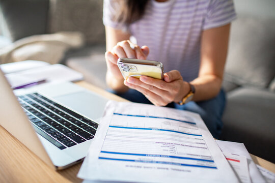 Woman using smartphone with laptop and documents on table