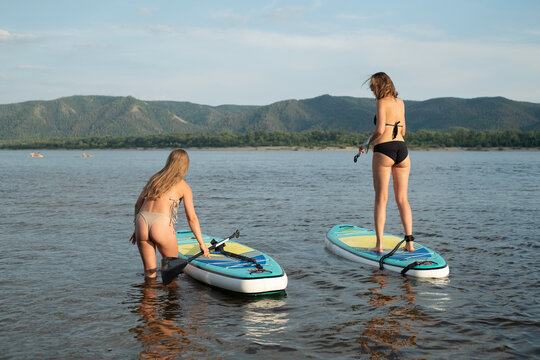 Two Women Enjoy Paddleboarding in Scenic Lake During Sunny Summer 