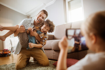 Father playing with son while being photographed by daughter at home